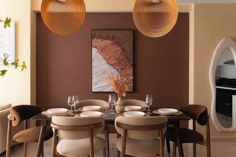Statement dining space featuring rich earth tones, designer pendant lights, and a mix of light and dark velvet chairs. Set for 6 guests with elegant tableware and a sculptural centerpiece. A warm, elevated setting for group dinners or celebrations.