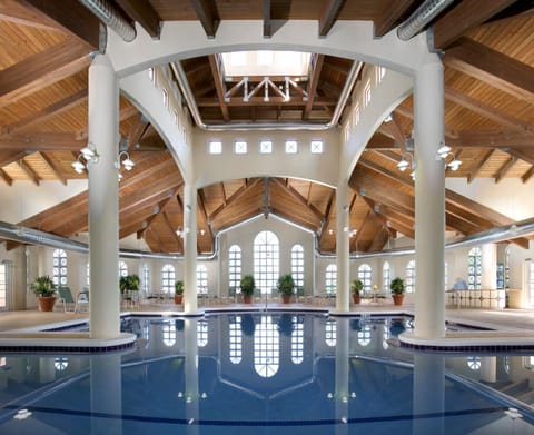 Indoor pool reflecting the wooden-beam ceiling, white columns, potted plants, and hanging light fixtures