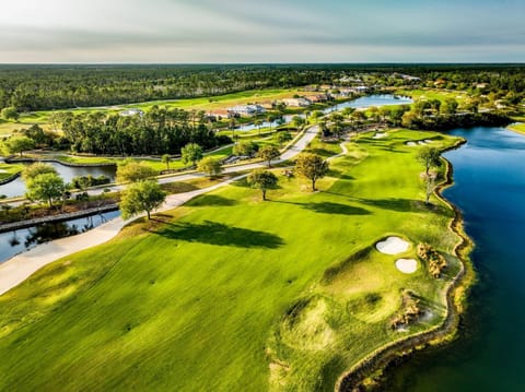 Aerial view of a golf course fairway with a water hazard, sand bunkers, and tree-lined residential buildings beyond