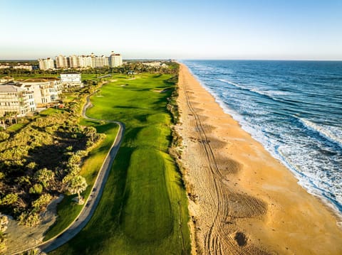 Aerial view of a golf course bordering the Atlantic, with beachfront towers beyond