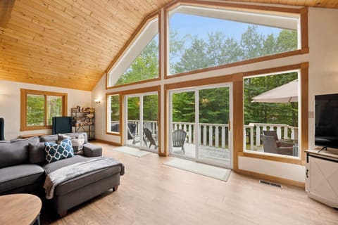 The vaulted wood ceiling and wall of windows keep the living area bright, with the sectional facing the gas fireplace and sliding doors opening to the deck.