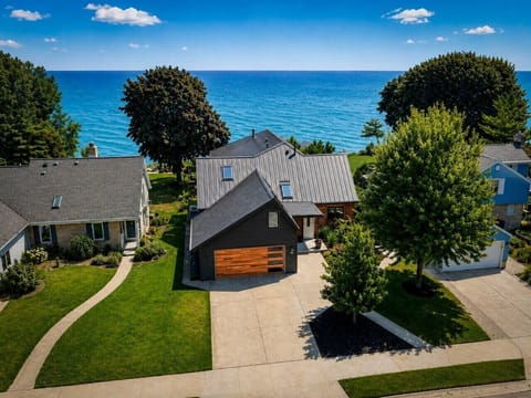 Captain’s Quarters is the dark modern home centered here, with Lake Michigan directly behind it. The setting is residential, with neighboring homes on both sides.