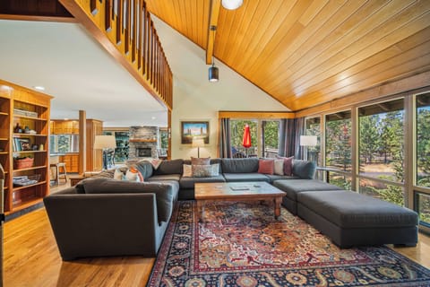 Sink into comfort in your spacious living room with soaring wood ceilings, plush seating, and wall-to-wall windows framing serene forest views—your perfect retreat after a day of adventure.