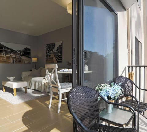 Woven bistro chairs wait on the balcony, offering a quiet spot for coffee in the fresh morning air. Large sliding doors bridge the gap between the sun-drenched outdoor patio and the airy, neutral living space inside.