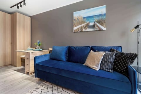 A comfortable living space centers around a vibrant blue couch with patterned pillows. A wooden wardrobe and a small dining set complete the room's layout.