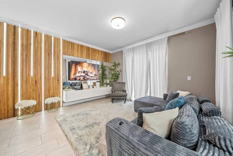 Welcome to a stylish living room with a chic navy sofa, textured pillows, and a stunning wooden accent wall. Enjoy the cozy warmth of the fireplace and the inviting natural light from large windows draped in soft curtains.