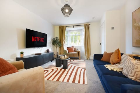 Bright and inviting living room featuring a comfortable sofa, two armchairs, a coffee table and a Smart TV. Large bay windows fill the space with natural light, creating an airy and relaxing atmosphere.