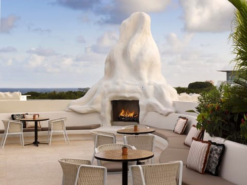 Outdoor terrace with a fireplace, low seating, and an abstract sculptural feature in the foreground