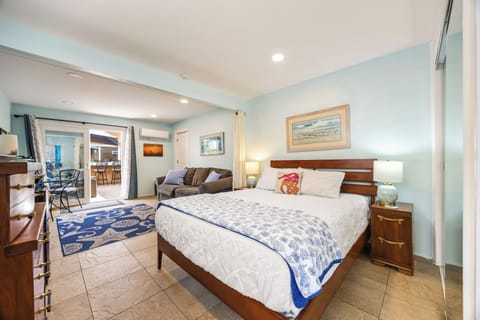 Comfortable Queen bed overlooking the open-concept living space and sunny patio access beyond.
