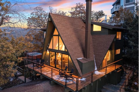 Cozy A-frame cabin exterior nestled among forest trees at dusk.