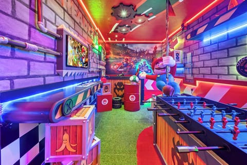 Step into a vibrant game room with neon lights and playful decor that spark nostalgia. Enjoy the lively atmosphere with a foosball table, fun wall art, and soft green turf, making it the ideal spot for relaxation and fun.