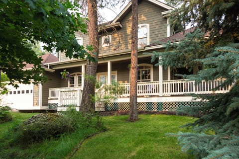 A charming two-story property nestled among mature trees and lush greenery, featuring welcoming wraparound porches and a peaceful natural setting.