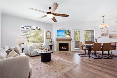 The living room's gas fireplace sets a cozy glow beside a mounted smart TV, with an open flow into the kitchen and dining area for easy gathering.