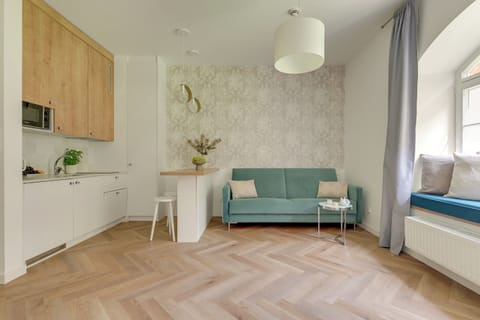 Jasny i przytulny salon z wygodną sofą, dużymi oknami i elegancką podłogą ułożoną w jodełkę. Delikatne dekoracje i stonowana kolorystyka tworzą harmonijną, komfortową przestrzeń do wypoczynku.