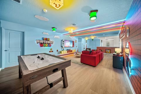 Welcome to a vibrant living area filled with playful decor and colorful lighting. Enjoy a match at the fun foosball table, relax in the cozy red seating, and soak in the energetic vibe created by the cheerful blue walls.