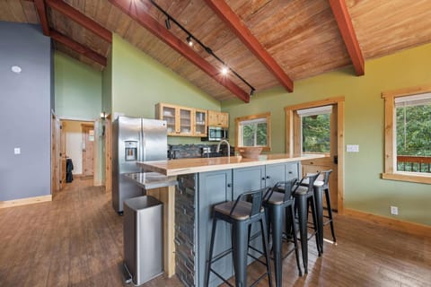 Gather around your spacious kitchen island with rich wood countertops and rustic charm. Natural light pours through generous windows, highlighting the soaring wooden ceiling beams and open-plan design perfect for shared meals and memories.