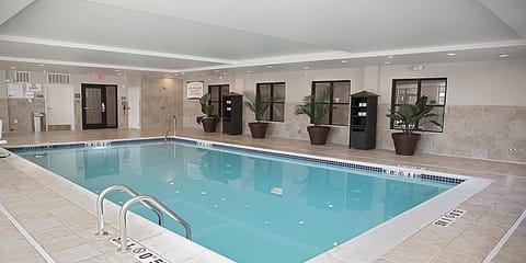 Indoor pool with tiled surround, metal entry steps, and large windows