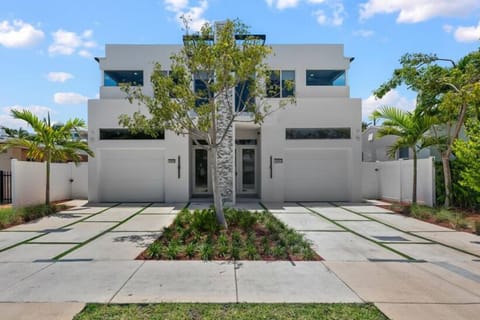 Modern multi-story home facade with paved driveway and lush landscaping.