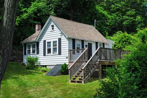Classic cottage exterior surrounded by lush greenery, with a spacious deck for relaxing outdoors.