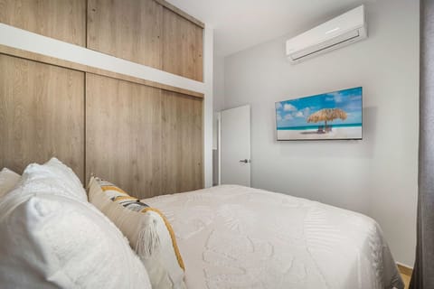 Comfortable second bedroom equipped with large custom wood wardrobes, a smart TV, independent A/C, and tropical-textured bedding.
