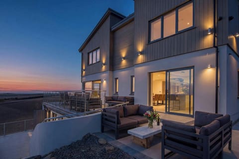 Modern house exterior at dusk with patio seating and lit wall lights