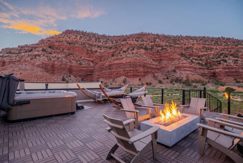 Sunset views from the rooftop deck—fire pit, private hot tub, and hammocks framed by Kanab's red rock cliffs.