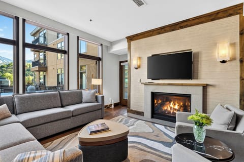 Cozy up by the fireplace in this bright living room, complete with plush seating, a large TV, and floor-to-ceiling windows.