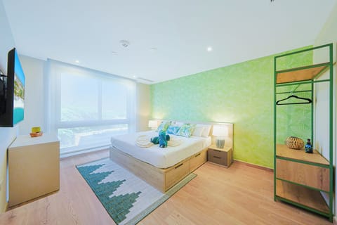 Sink into your serene retreat where a plush bed awaits beneath natural light from floor-to-ceiling windows. The vibrant accent wall and warm wood tones create a tropical-inspired escape perfect for unwinding after a day of adventure.