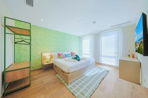 Wake up in a bright, inviting bedroom featuring a plush king-size bed, tropical-inspired wallpaper, abundant natural light, and a sleek open clothing rack for added convenience.