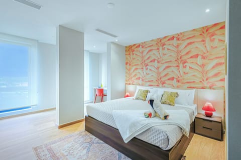 Spacious bedroom with crisp linens, tropical accent wall, and ocean views through floor-to-ceiling windows. Soft bedside lighting creates a serene, resort-style retreat.