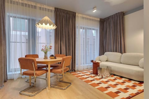 Elegancki i przytulny salon z wygodną sofą oraz stylową strefą jadalnianą. Ciepłe oświetlenie, drewniane akcenty i dekoracyjny dywan tworzą wyjątkową, harmonijną przestrzeń idealną do relaksu i wspólnego spędzania czasu.