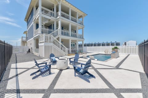 A spacious three-story coastal retreat featuring a private pool, poolside loungers, and Adirondack seating around the fire pit. Expansive balconies provide additional outdoor seating and elevated views, while the fenced yard offers added privacy.