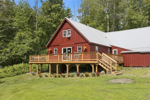 The wraparound deck hugs the front of the home, with steps down to a grassy, tree-lined yard that keeps things private.