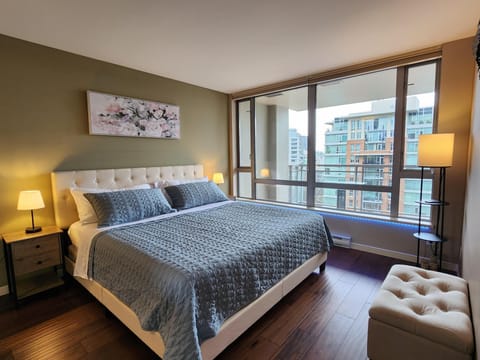 King bed with a tufted white headboard, two wooden nightstands with lamps, and floor-to-ceiling windows.