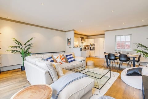 Open plan living room with kitchen and dining table. Opening onto large balcony terrace, which has outdoor seating.