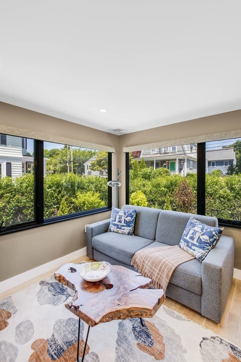 Sunlit lounge area featuring a grey sofa, live-edge wood coffee table, patterned area rug, and dual-aspect windows.