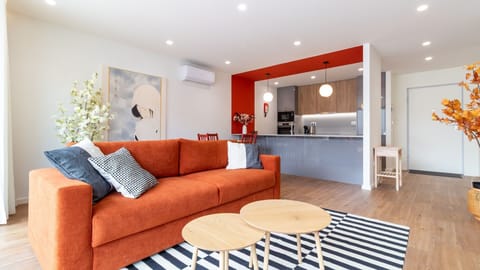 Relax in the vibrant living area with an inviting orange sofa, perfect for unwinding after a day of exploring, while the open-plan kitchen makes preparing meals and entertaining a breeze. Enjoy the bright, modern space designed for comfort and convenience