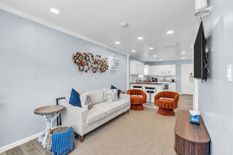 Bright open living room with modern seating, TV, and full kitchen