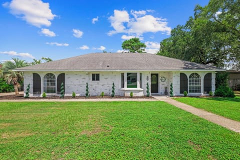 Your beach getaway starts here — a sunny, white-brick ranch with a manicured lawn and spiral topiaries lining the walkway.