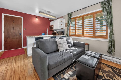 Sink into plush seating in your open living space, where warm red accent walls and natural light through plantation shutters create a cozy retreat. The kitchenette is steps away for easy meal prep.