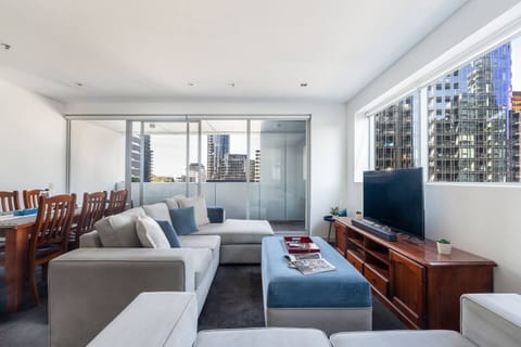 Settle into the living area, where generous seating and soft natural light create an inviting space to relax, with a TV for easy evenings and city views just beyond the windows.