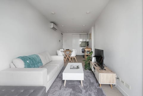 Settle into the living area where a sofa and TV create a simple space to relax, with natural light softening the clean, uncluttered layout.