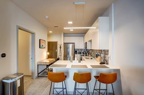 First-floor apartment featuring a modern kitchen with stainless steel appliances, a bright breakfast bar with three leather stools, and warm lighting—ideal for relaxed dining or entertaining.