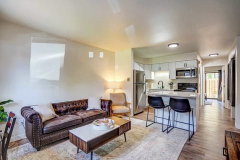 Bright and stylish open-concept living area with a leather sofa, modern décor, and a full kitchen featuring stainless steel appliances—perfect for relaxing or enjoying a home-cooked meal during your stay.