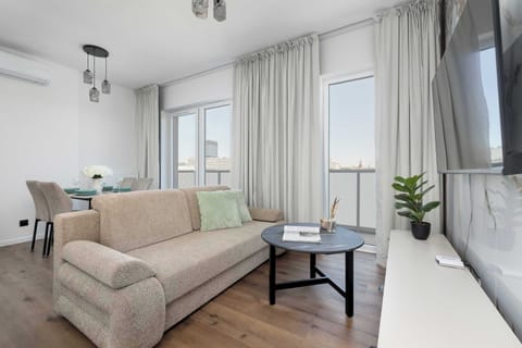 Bright living room with a comfortable sofa, coffee table, TV, and large windows providing plenty of natural light.