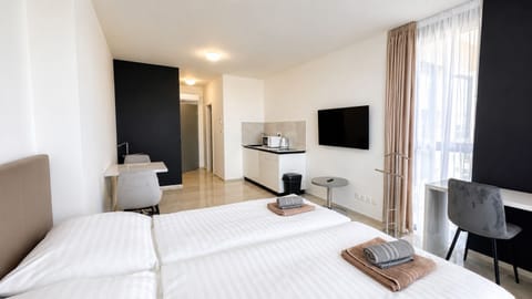 Bright modern studio with twin beds, kitchenette, and large windows