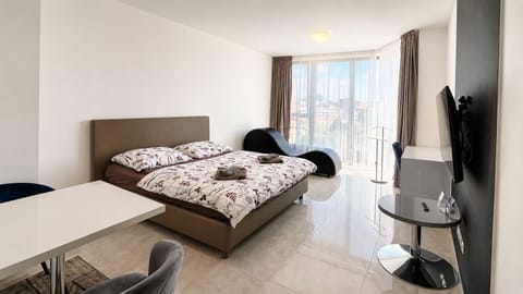 Bright modern bedroom with balcony views, workspace, and cozy lounge chair