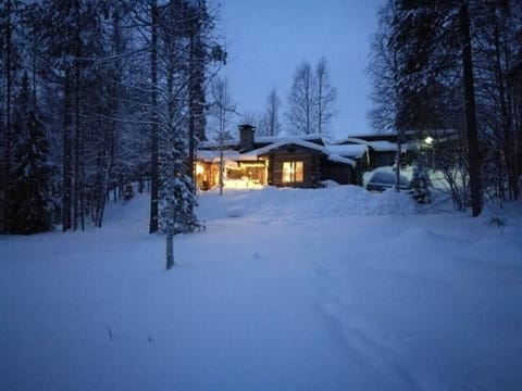 The log cabin lit up on a winter evening, surrounded by deep snow and pine trees.