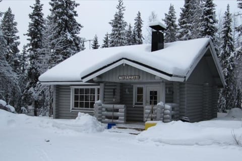 Traditional log cabin surrounded by snow-covered pine forest.