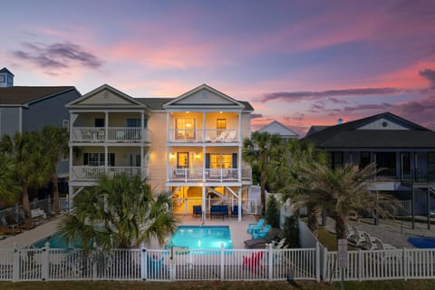 Stunning beachside property featuring multiple balconies and a private pool, surrounded by tropical palms under a breathtaking sunset sky.